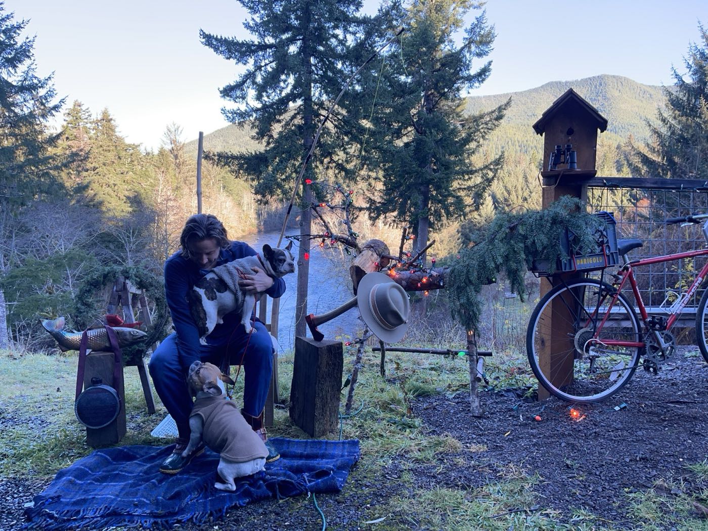 David seated outdoors on the Olympic Peninsula in winter, with Stella and Jackson, near a small wreath shrine